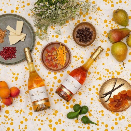 Zwei Flaschen Gran Tokaj Tokaji Aszú Wein umgeben von Aprikosen, Birnen, Feigen, Vanilleschoten, getrockneten Aprikosen, Feigen.