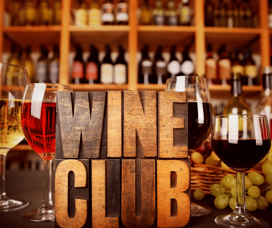 Holzbuchstaben bilden den Text 'WINE CLUB' im Vordergrund. Im Hintergrund sind mehrere Weingläser mit verschiedenen Weinen und eine Regalwand mit Weinflaschen sichtbar.