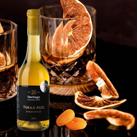 Flasche Heritage Tokaji Aszú 6 Puttonyos 2015 mit zwei Gläsern, getrockneten Orangenscheiben und Aprikosen