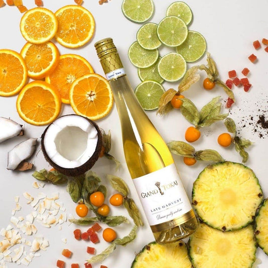 Flasche Grand Tokaj Late Harvest Wein umgeben von Orangenscheiben, Limettenscheiben, Kokosnuss, Physalis, Ananasscheiben