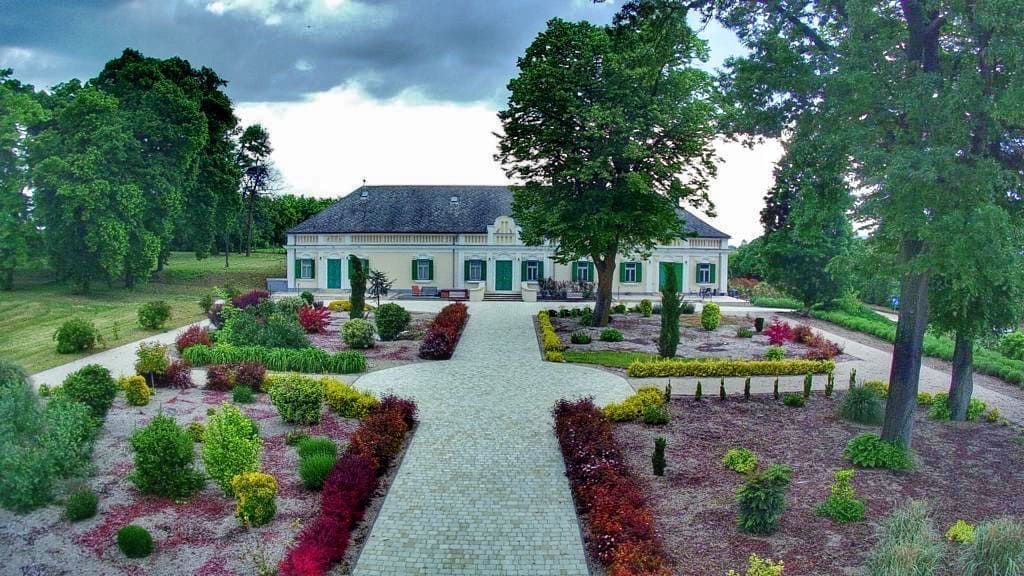 Das Kurhaus St. Gaal mit grünem Garten und bunten Blumenbeeten, umgeben von Bäumen. Ein gepflasterter Weg führt zur Eingangstür.
