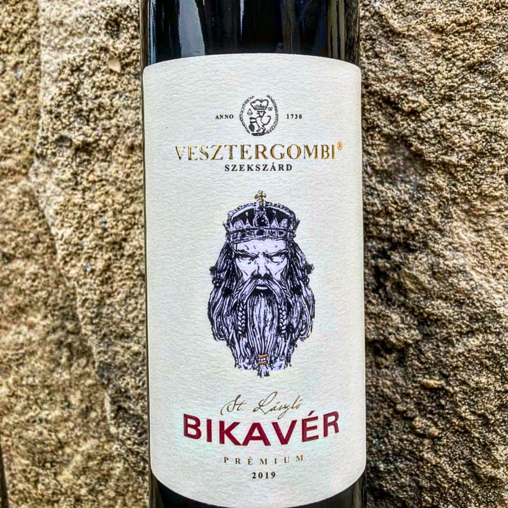Eine Flasche Rotwein mit einem weißen Etikett. Das Etikett zeigt den Text 'VESZTERGOMBI SZEKSZÁRD' und 'BIKAVÉR PREMIUM 2019' sowie ein Wappen mit einem Löwenkopf.