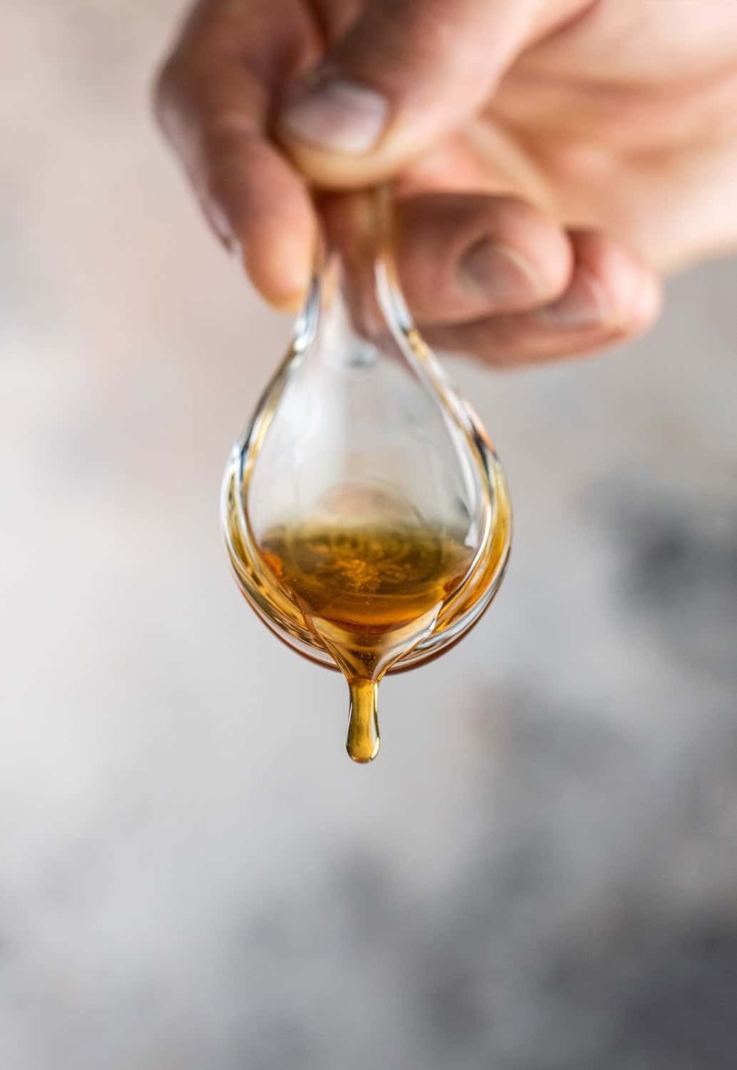 Eine Hand hält einen Tropfer mit goldbraunem Tokaji Essenz, aus dem ein Tropfen herabfällt.
