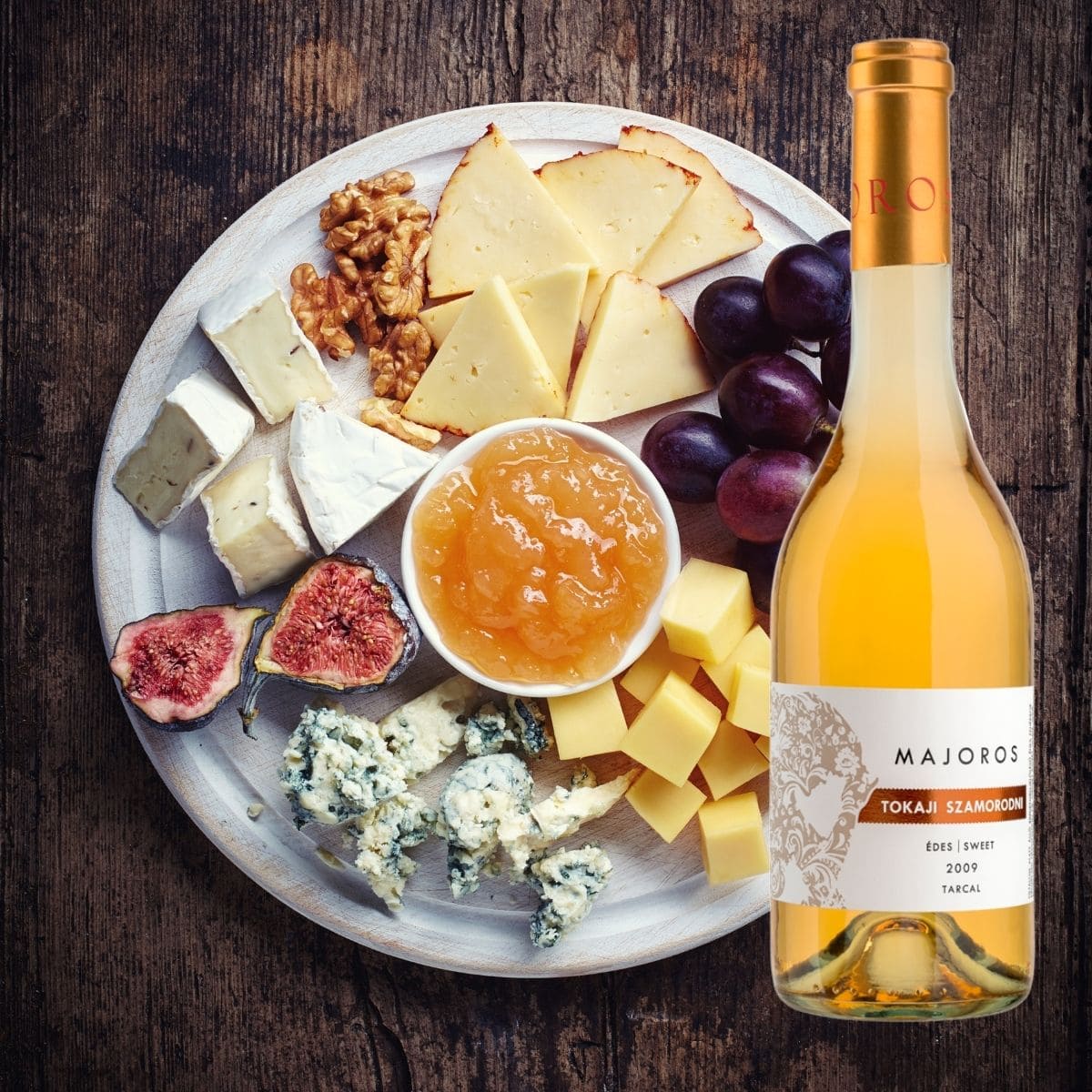 Käseplatte mit verschiedenen Käsesorten, Feigen, Walnüssen, Marmelade neben einer Flasche Majoros Tokaji Szamorodni Süss
