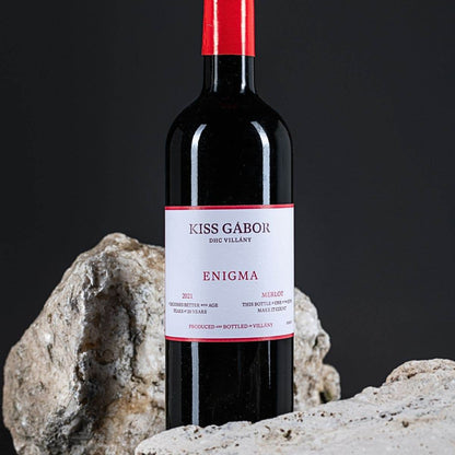 Flasche Kiss Gábor Enigma Merlot 2021 mit rotem Verschluss, umgeben von zwei großen Steinen auf schwarzem Hintergrund