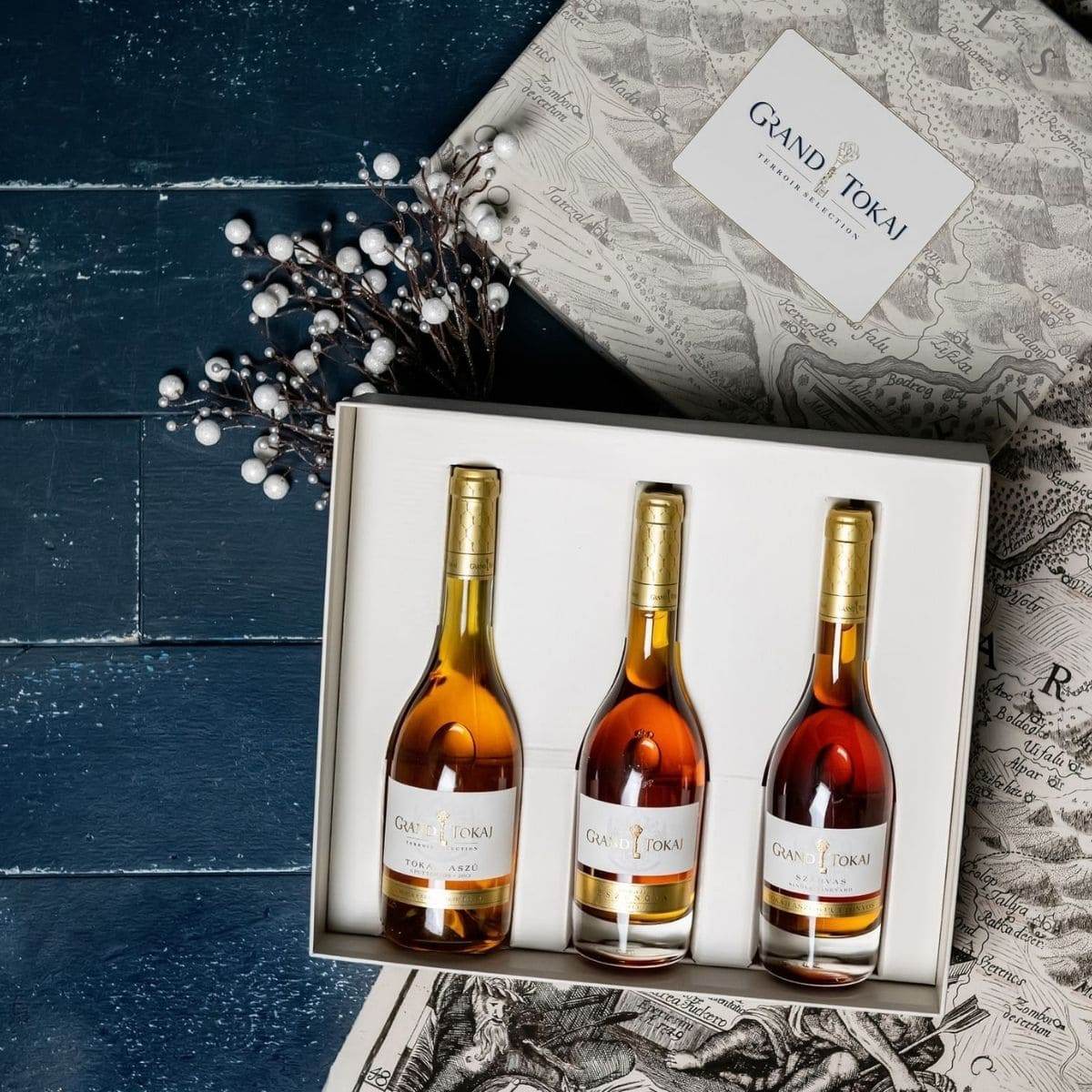 Drei Flaschen Grand Tokaj Aszú Wein in einer Geschenkbox mit Landkartenmuster und goldenen Verschlüssen