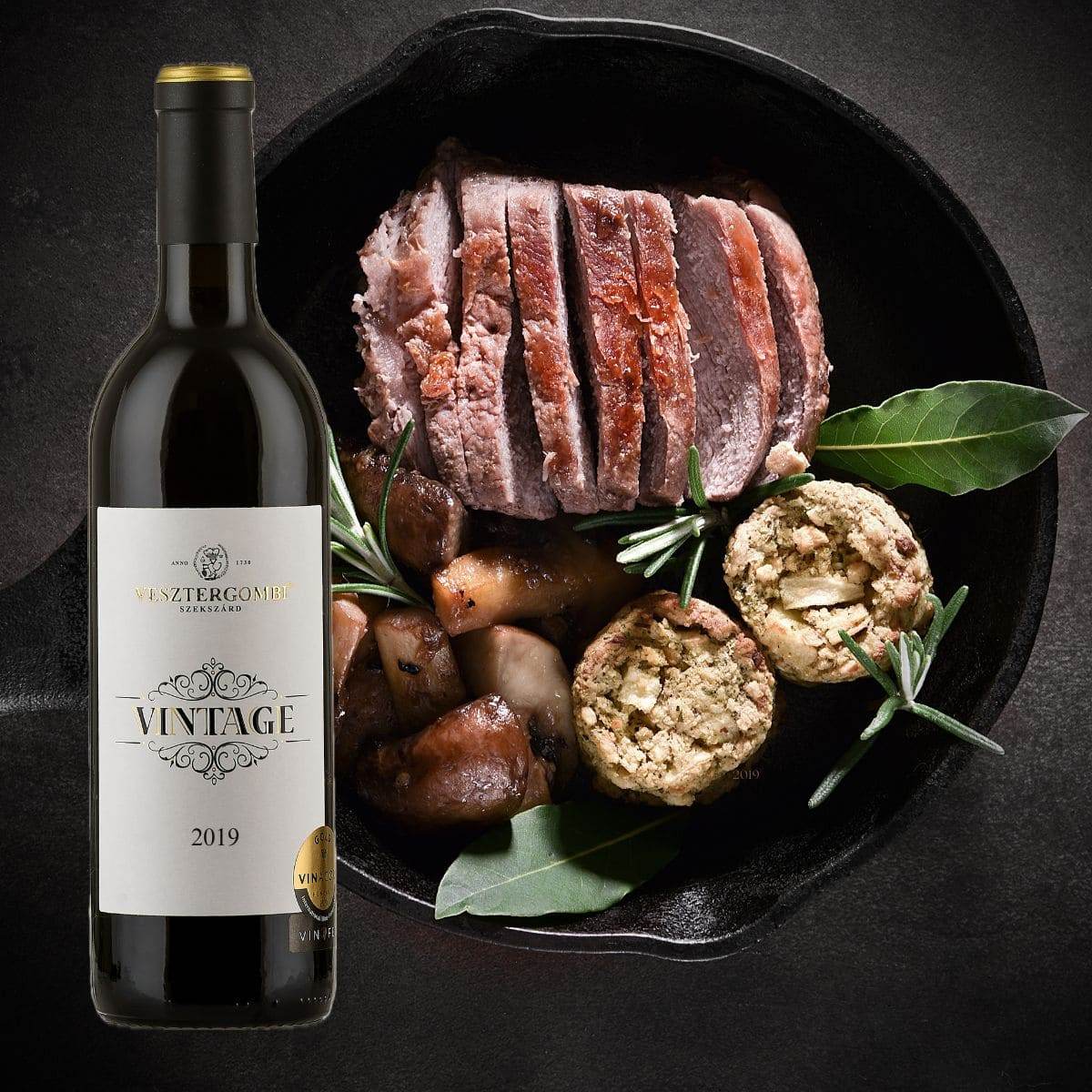 Flasche Vesztergombi Vintage 2019 Rotwein neben gebratenem, in Scheiben geschnittenem Fleisch mit Pilzen, Kräutern & Klössen.