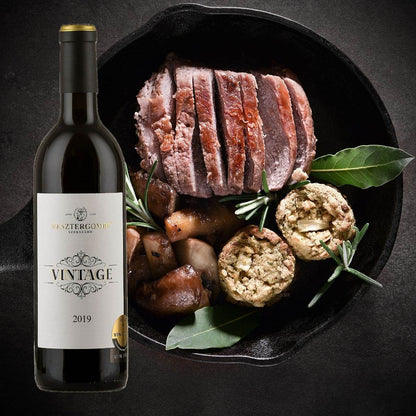 Flasche Vesztergombi Vintage 2019 Rotwein neben gebratenem, in Scheiben geschnittenem Fleisch mit Pilzen, Kräutern & Klössen.