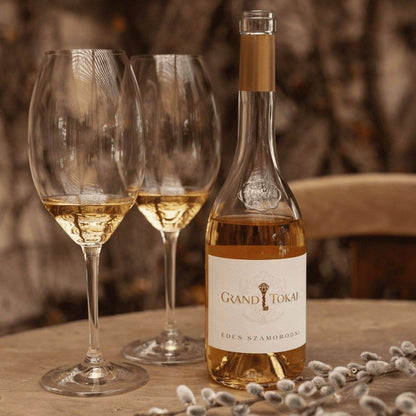Flasche Grand Tokaj Édes Szamorodni Weisswein und zwei gefüllte Weingläser auf einem Holztisch mit Weidenkätzchen