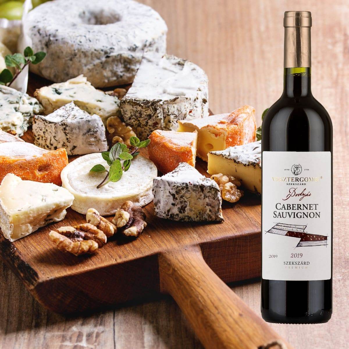 Verschiedene Käsesorten und Walnüsse auf einem Holzbrett neben einer Flasche Vesztergombi Bodzás Cabernet Sauvignon Rotwein