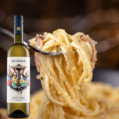 Gabel mit Spaghetti Carbonara vor unscharfem Hintergrund und Flasche Solaris-Wein mit farbigem Etikett im Vordergrund