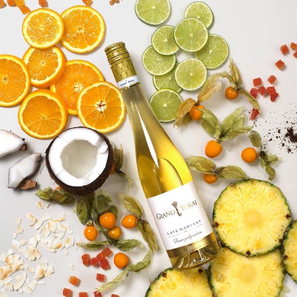 Flasche Grand Tokaj Late Harvest Wein umgeben von Orangenscheiben, Limettenscheiben, Kokosnuss, Physalis, Ananasscheiben