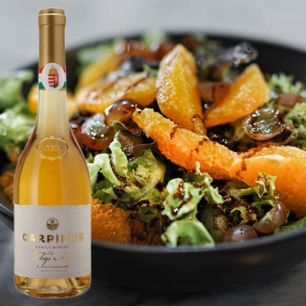Flasche Carpinus Weißwein neben einem Salat mit Orangenfilets, Trauben und grünem Blattsalat, garniert mit Balsamico-Dressing