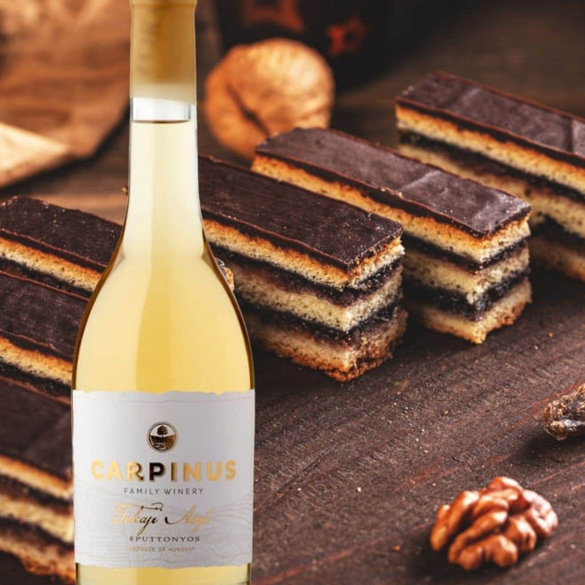 Flasche Carpinus Tokaji Aszú Weisswein vor mehreren Gerbeaud Schnitten mit Schokoladenschicht und Walnüssen auf dunklem Holz