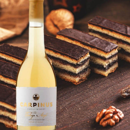 Flasche Carpinus Tokaji Aszú Weisswein vor mehreren Gerbeaud Schnitten mit Schokoladenschicht und Walnüssen auf dunklem Holz