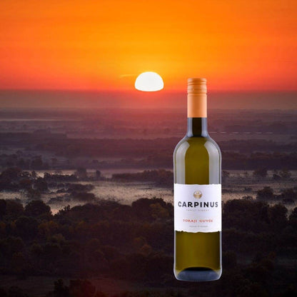 Flasche Carpinus Tokaji Cuvée Weisswein vor einem orangefarbenen Sonnenuntergang über einer bewaldeten Landschaft