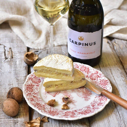 Weisswein Carpinus Tokaji Hárslevelű in Flasche und Glas neben einem Teller mit geschnittenem Weichkäse und Walnussschalen