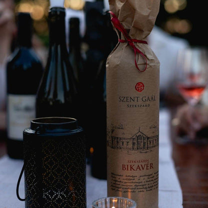 Flasche Szent Gaál Szekszárd Bikavér Rotwein in brauner Papierverpackung mit rotem Band, umgeben von weiteren Weinflaschen un