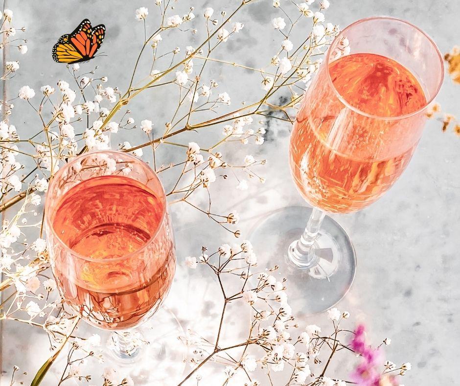 Zwei mit roséfarbenem Getränk gefüllte Sektgläser auf Marmoroberfläche mit zarten weißen Blütenzweigen und einem Schmetterling