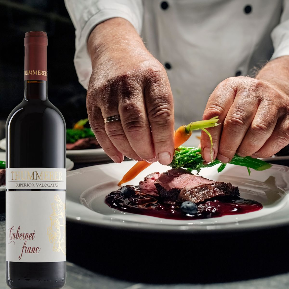 Hände eines Kochs garnieren ein Stück Fleisch mit Sauce, Karotten und grünem Gemüse auf einem weißen Teller neben einer Flasche Thummerer Cabernet Franc Wein