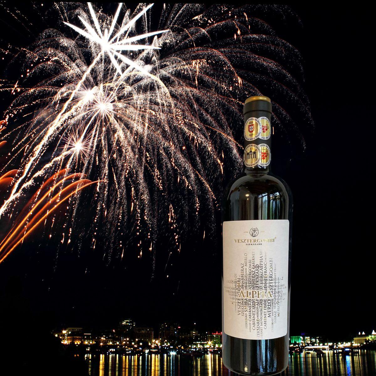 Flasche Vesztergombi Alpha Rotwein vor Nachthimmel mit Feuerwerk über einer beleuchteten Stadt am Wasser
